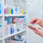 Pharmacist using a tablet in front of pharmacy shelves