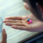 Man holding a glass of water and looking at the pills in his other hand