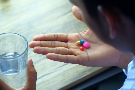 Man holding a glass of water and looking at the pills in his other hand