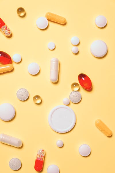 Various colorful pills, tablets, and capsules scattered on a yellow background