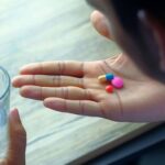 A close-up of a person holding colorful pills in their open palm while holding a glass of water.