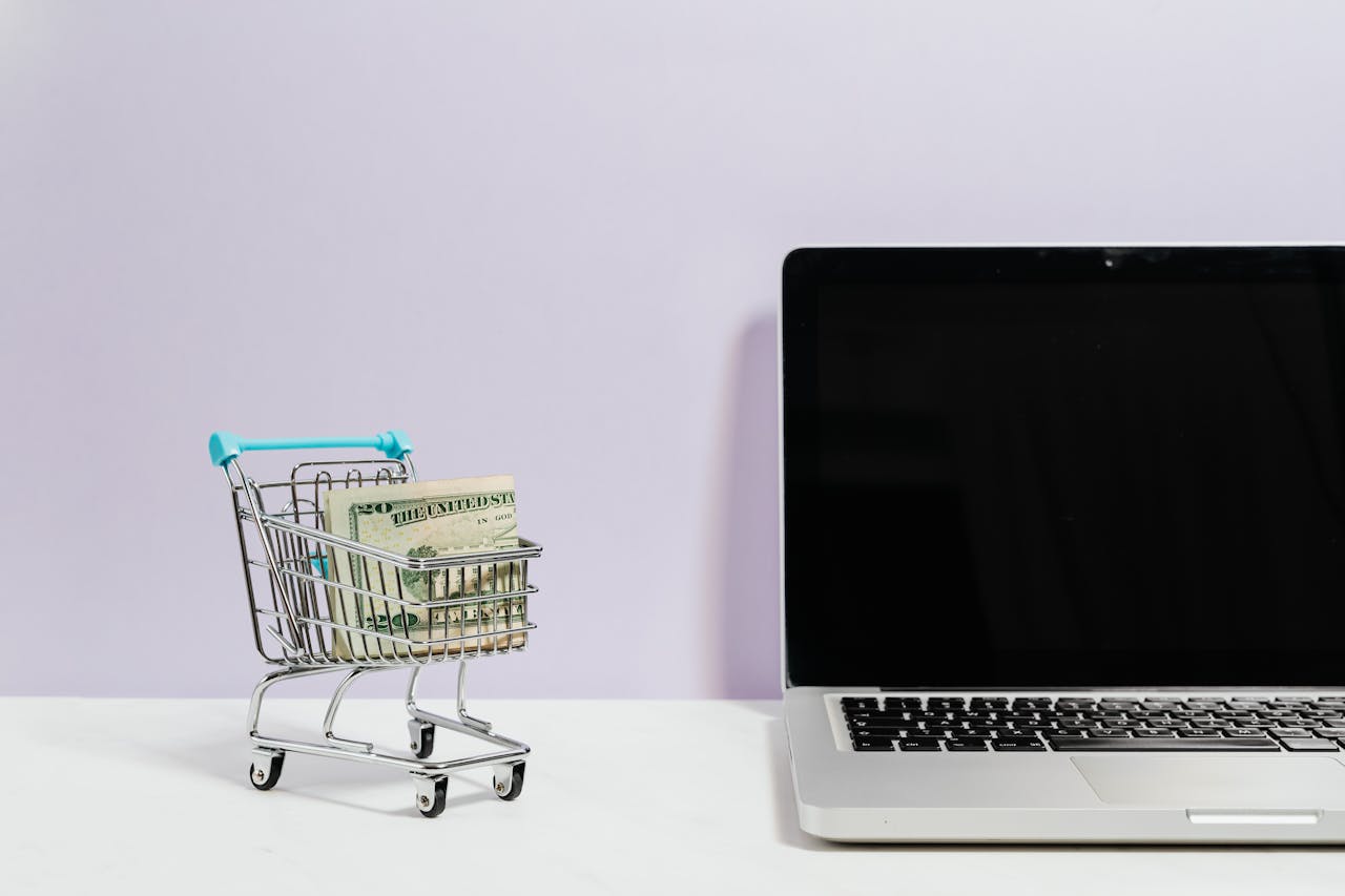 A tiny shopping cart carrying money next to a computer