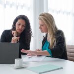 A woman demonstrating pharmacy software on a tablet to a pharmacist in a one-on-one meeting