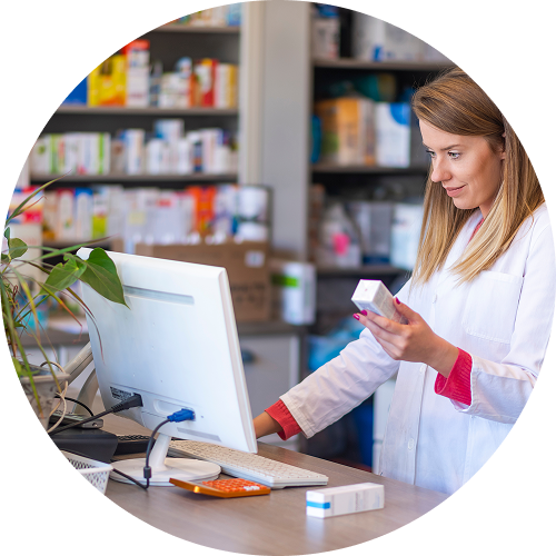 A pharmacist holding a medicine box in one hand while looking at a computer screen