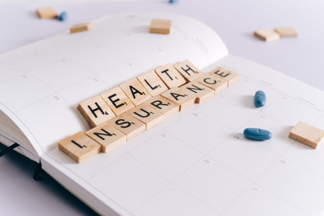 A daily business planner with scrabble tiles spelling “health insurance” and scattered pills