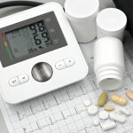 A digital blood pressure monitor, assorted pills, and pill bottles displayed on top of an electrocardiogram printout.