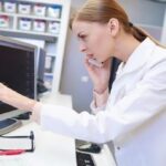 A female pharmacist on the phone looks at a report on a computer screen