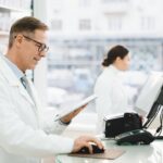A pharmacist consulting a tablet while using pharmacy software
