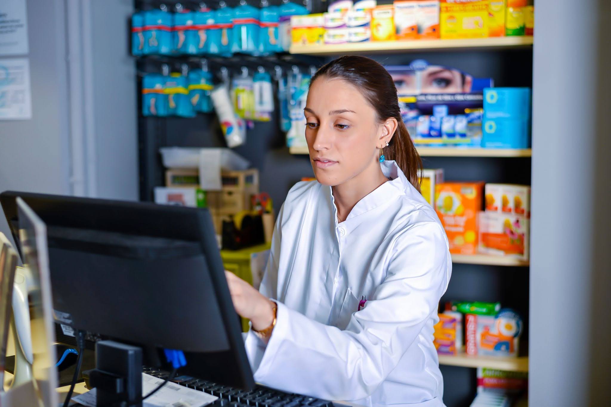 independent-pharmacy-staff-using-pharmacy-software-and-pos-system Pharmacist using pharmacy software at a workstation in an independent pharmacy