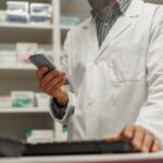 Pharmacist using pharmacy software with patient mobile app and delivery dashboard open